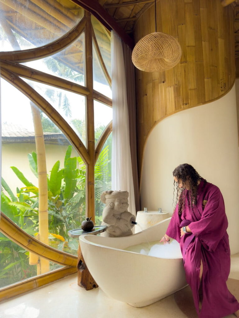 Sally in her burgundy robe sitting on the bath tub full of soap in my private villa inside the Udaya Bali