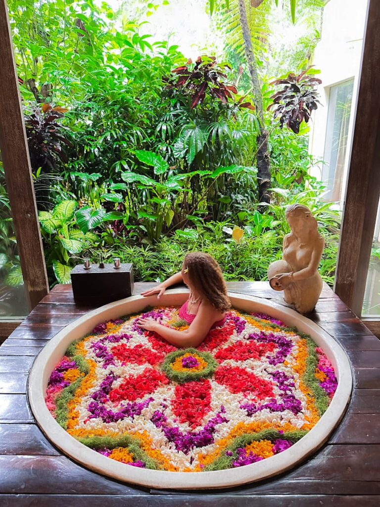 Sally is sitting in he famous flower bath at Kaveri Spa at The Udaya Hotel & Spa Ubud Bali its colourful petals, jungle views, and such a special experience.