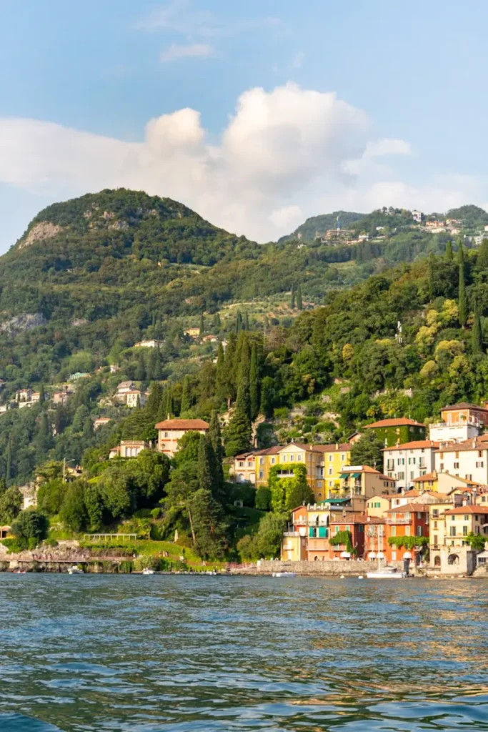 Warm coloured lakeside homes sit at the edge of Lake Como Italy backed by a forested mountain