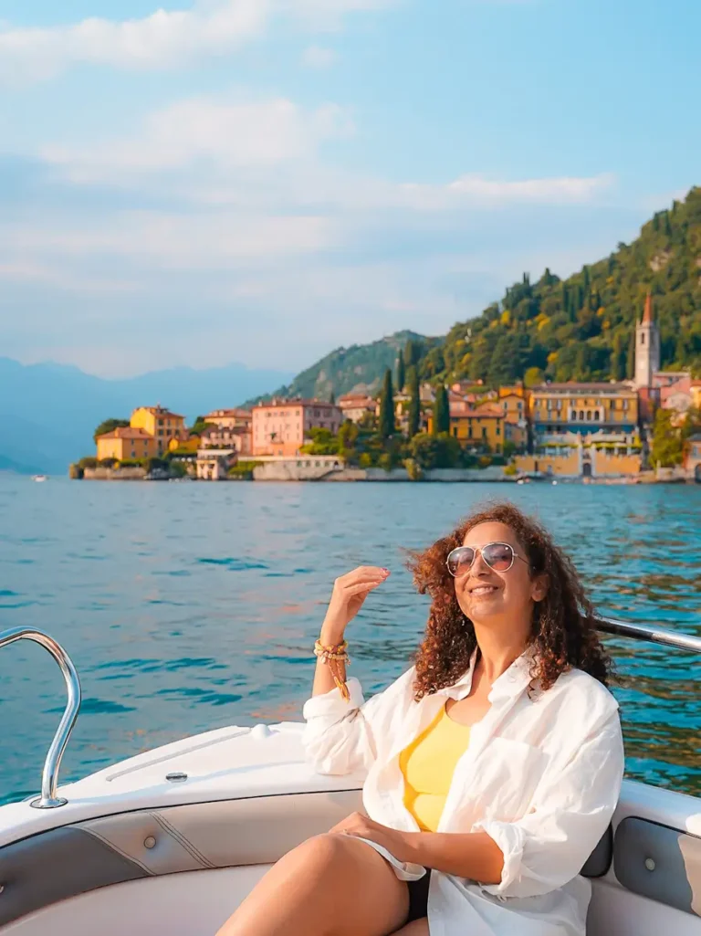 4 Best Boat Tours In Lake Como: Elegant Ways to Explore Italy’s Most Iconic Lake Woman sitting on the front of a private boat on Lake Como Italy with pastel houses behind her.