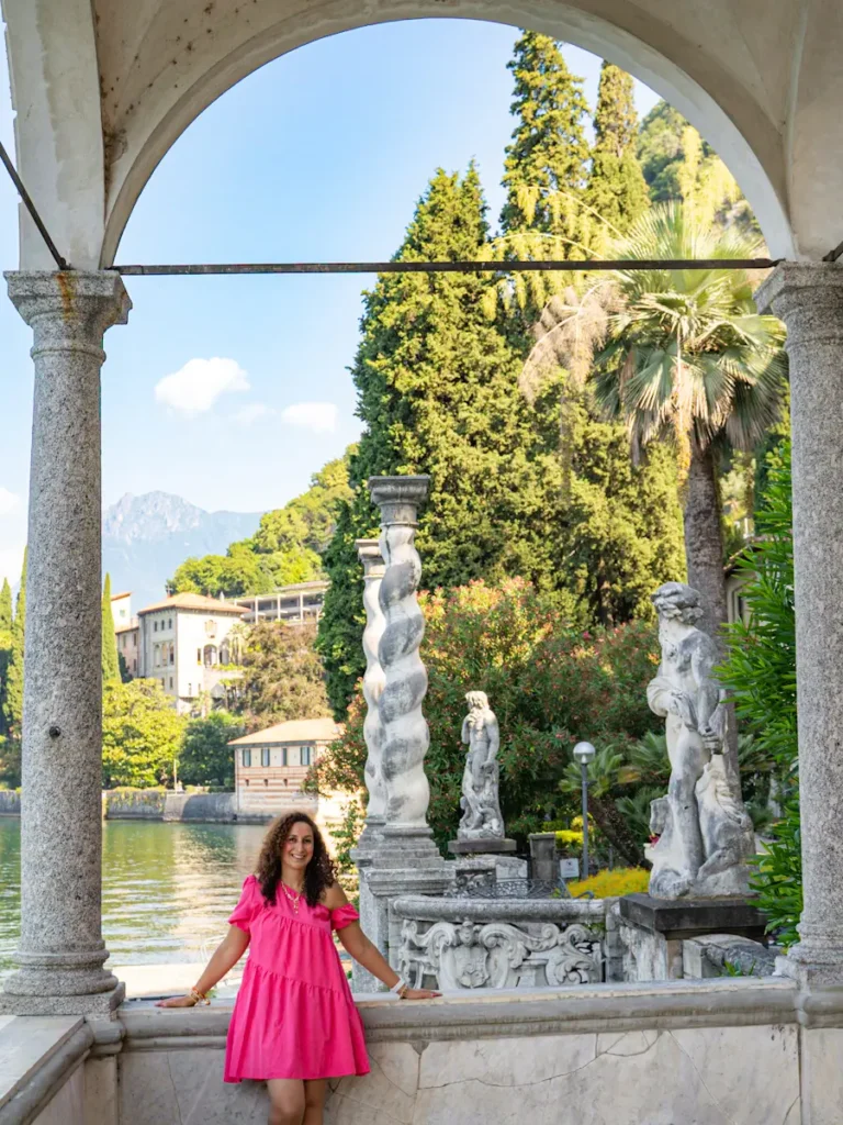 Woman in a pink dress in Villa Monastero standing under a vine covered archway overlooking the beautiful gardens of Lake Como Italy.