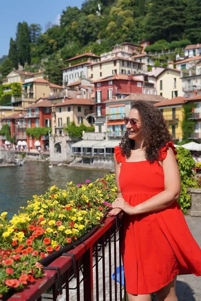 Woman in a red dress sitting by colorful flowers in Varenna Lake Como Italy during her 1 day lake como trip from Milan