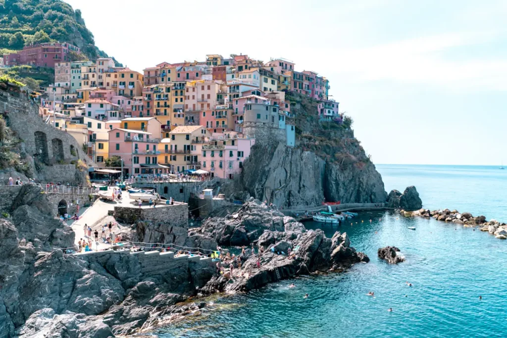 View of Manarola in Cinque Terre, Italy, with colorful cliffside buildings stacked above turquoise sea waters and rocky coastline