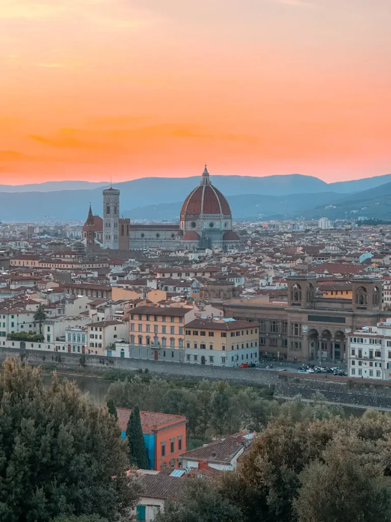 Florence glows at sunset as the sky turns orange above the historic skyline and cathedral dome. Watching the city from above is one of the most magical things to do in Florence