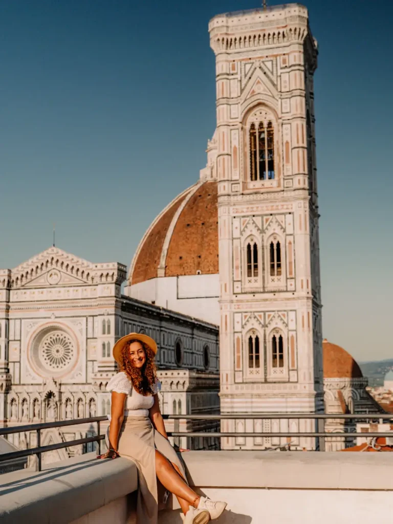 Florence 3 Days Itinerary: A Perfect Guide For First Timers women sitting on a rooftop hotel in florence italy and the view of the duomo in the background with blue skies