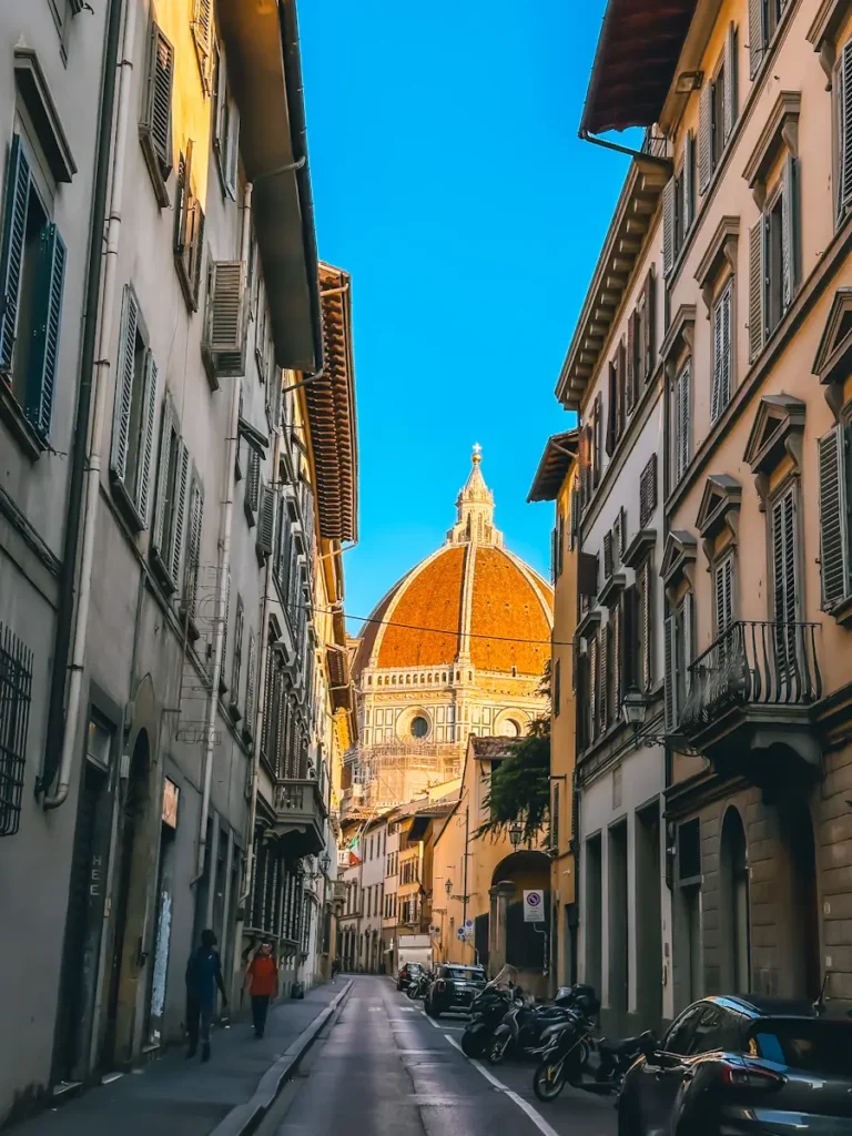 Narrow historic street in Florence Italy with tall buildings and blue sky overhead.