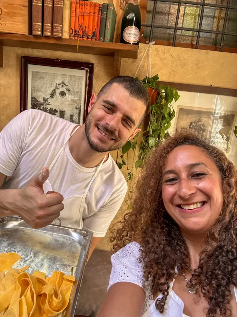 Girl smiling and taking a selfie with an Italian chef holding a tray of fresh pasta during a Florence, Italy pasta making class, a must-do activity in a Florence itinerary