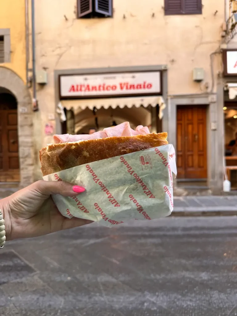 Florence 3 Days Itinerary: A Perfect Guide For First Timers a hand of a woman holding panini sandwich in the street infront of the famous panini shop all' antico Vinaio in Florence italy