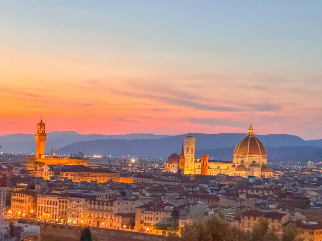 Sunset over Florence with warm orange light washing over the skyline and cathedral dome. The glowing horizon creates a romantic atmosphere perfect for a Florence itinerary