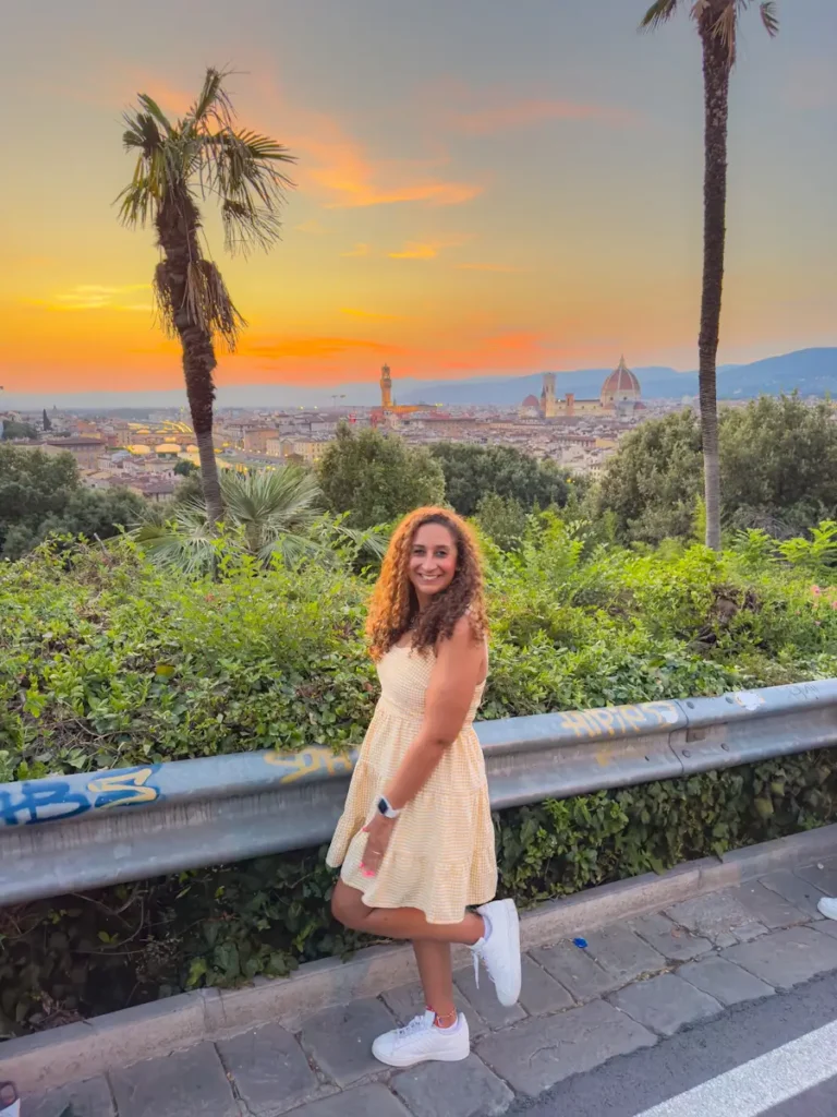 A woman stands at a scenic overlook as the sun sets over Florence, the Duomo visible in the distance. This viewpoint is a must stop on any Florence itinerary for golden hour photos