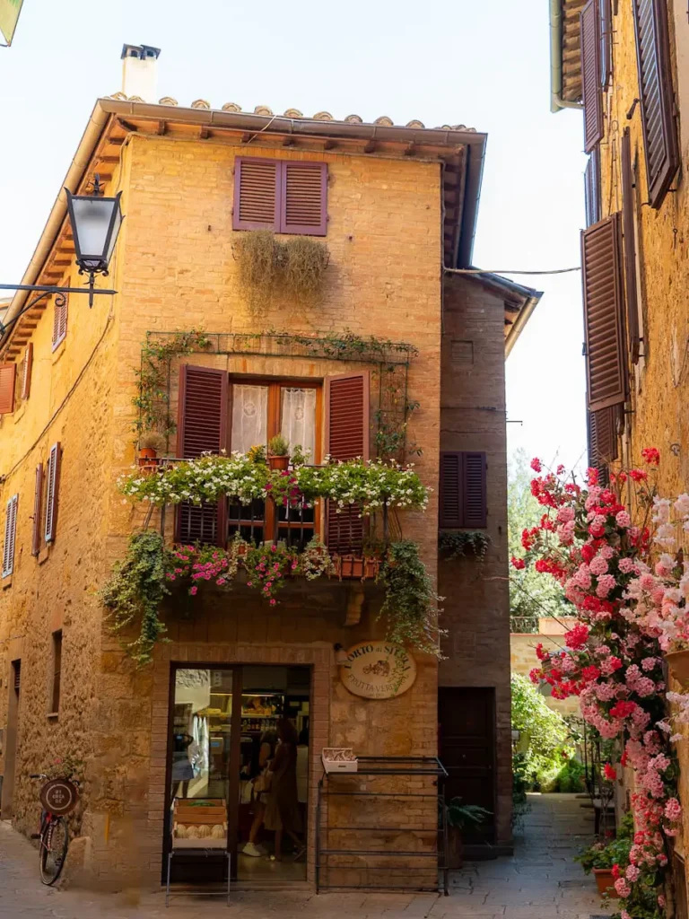 Golden building in Pienza, Tuscany, Italy, adorned with flowers and a shop on the ground floor, captured during a day trip from Florence