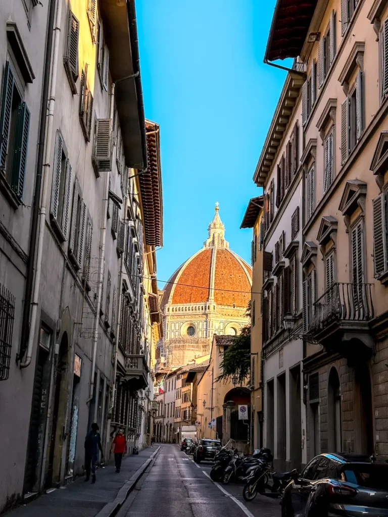 Narrow street view in Florence Italy featuring a tall historic tower and warm-toned buildings. The perspective emphasizes the charm of the surrounding neighborhood