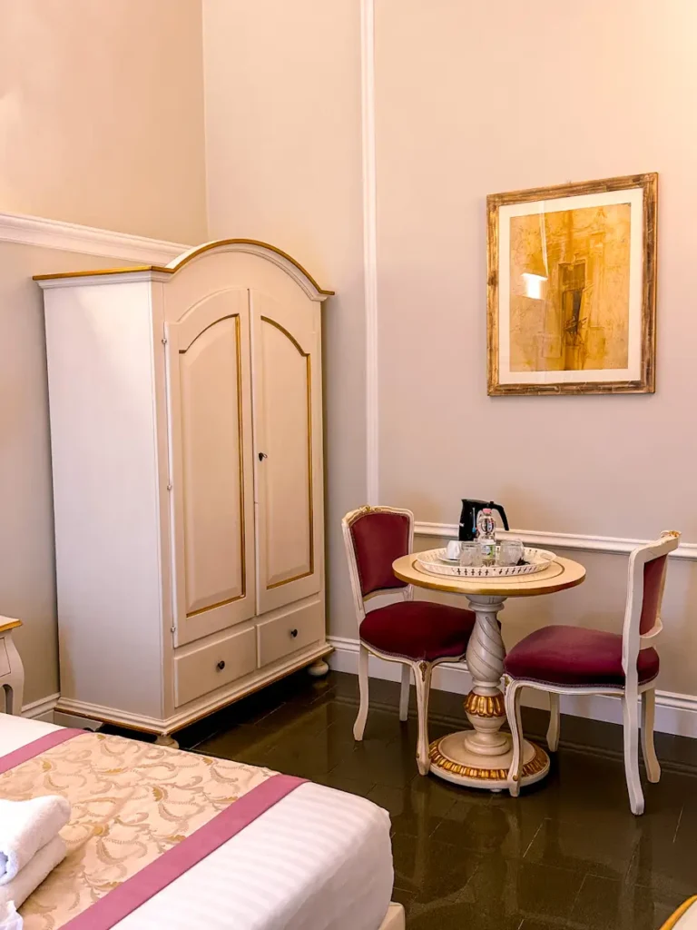 Small sitting area inside a hotel room with a wardrobe, round table, and chair, styled in warm beige tones. The setup suggests a functional and intimate space within the B and b la terraza sul duomo stay in florence italy.
