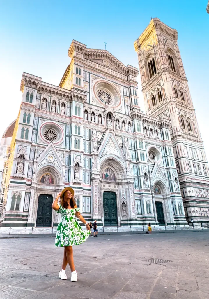 woman wearing green and white dress standing infront of Florence Cathedral in Florence Italy captured from the square with detailed facade and open space in front. 
