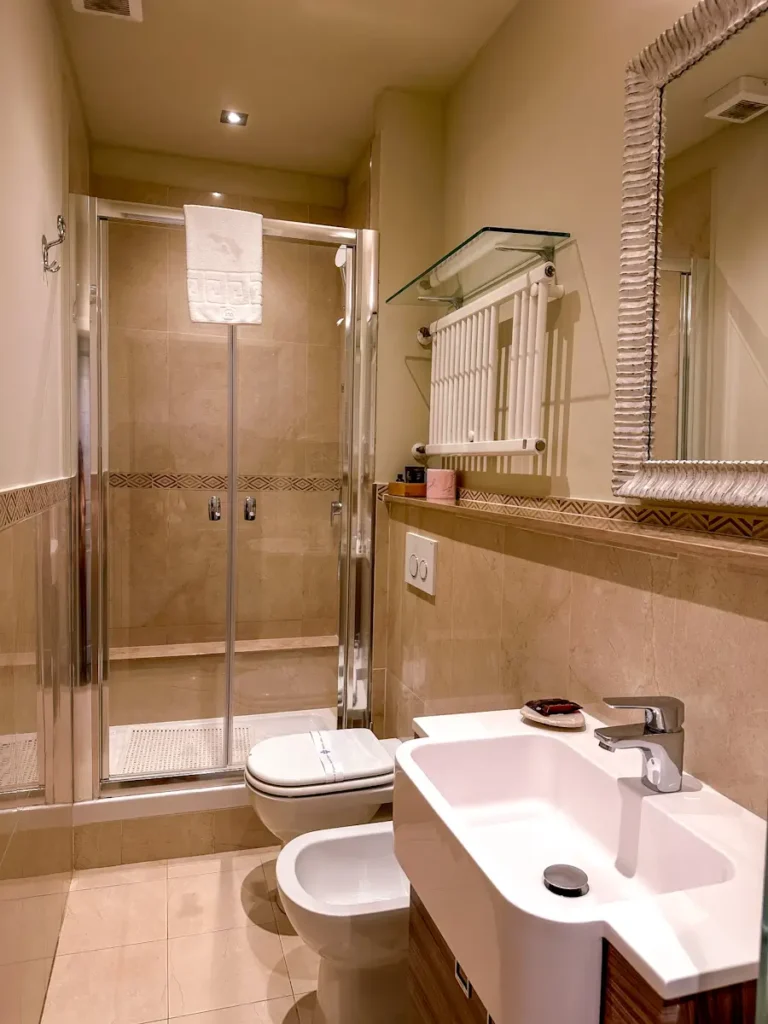 Modern bathroom in Florence Italy with a glass shower, white sink, and mirror under warm lighting. Clean design and compact layout highlight amenities included in the accommodation.