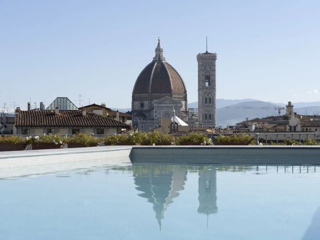 swimming pool in Grand Hotel Minerva with background of Florence Italy skyline with the large domed Duomo cathedral and the Grotto tower rising above a cluster of historic buildings. The sky is soft and blue
Grand Hotel Minerva  is one of the best florence hotels with pool