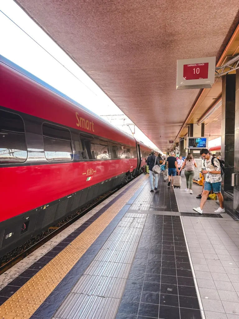red and black coloured train in the station in Italy and some peoples are standing in the platform waiting to board the train