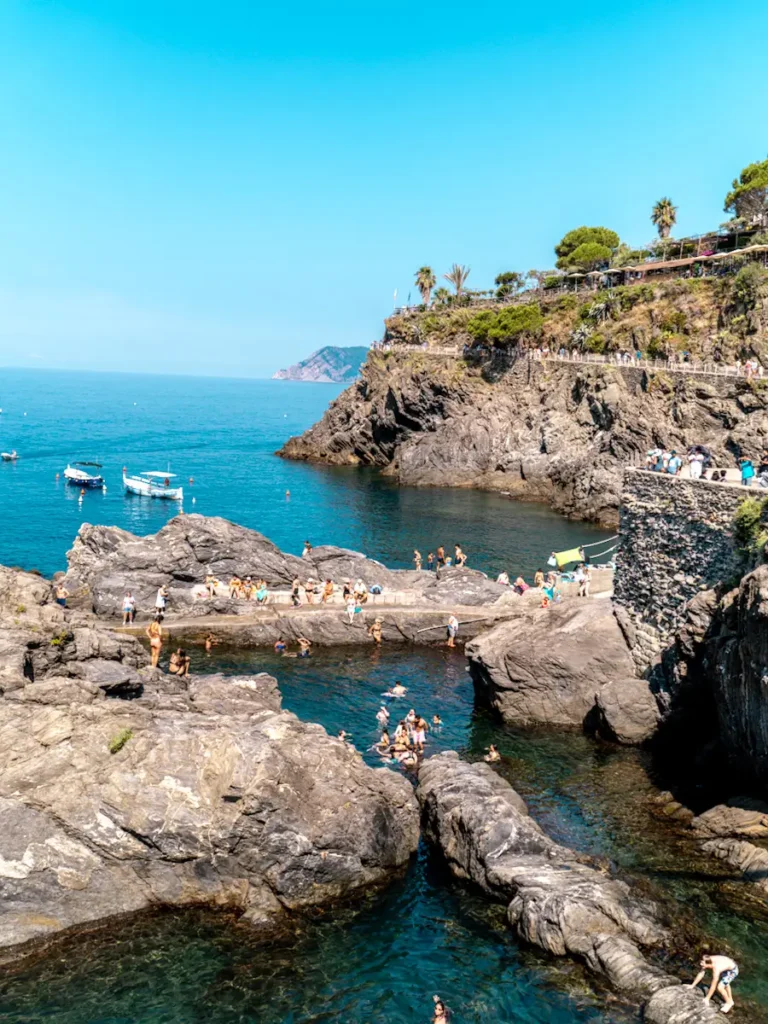 Best Cinque Terre Tour From Florence: Review & My Experience Rocky coastline with clear turquoise water, rugged cliffs, and sunny blue skies in Manarola, Cinque Terre Italy